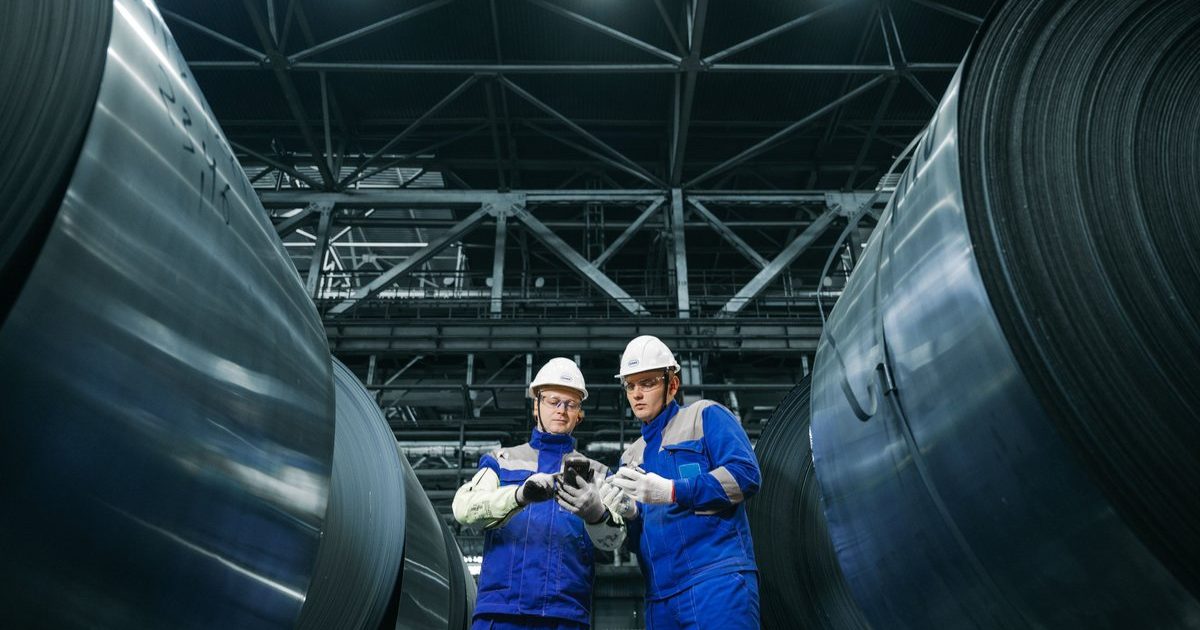 Two inspectors checking records on a phone between steel coils